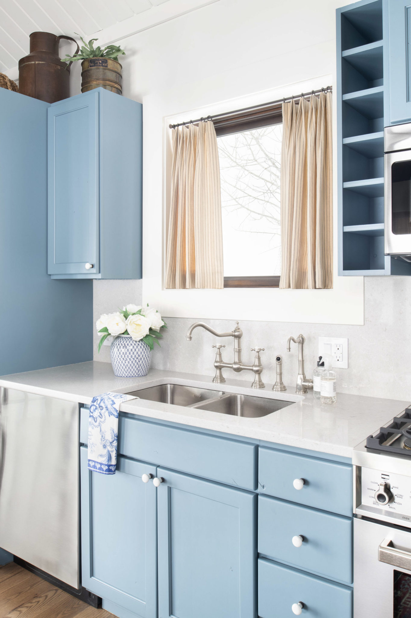 Sky blue kitchen cabinets with white walls and tan curtains